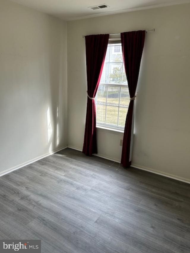 empty room with baseboards, visible vents, and wood finished floors