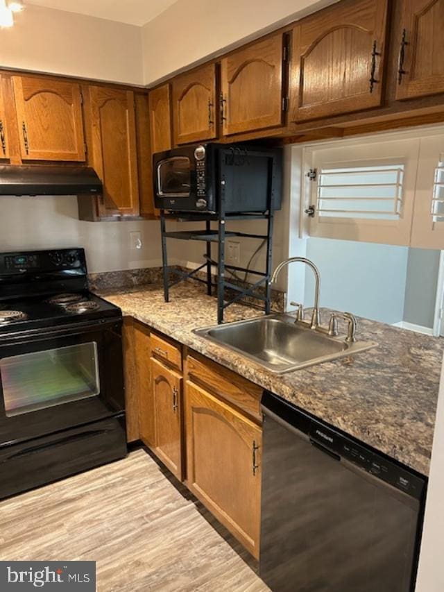 kitchen with under cabinet range hood, a sink, brown cabinets, black appliances, and light wood finished floors