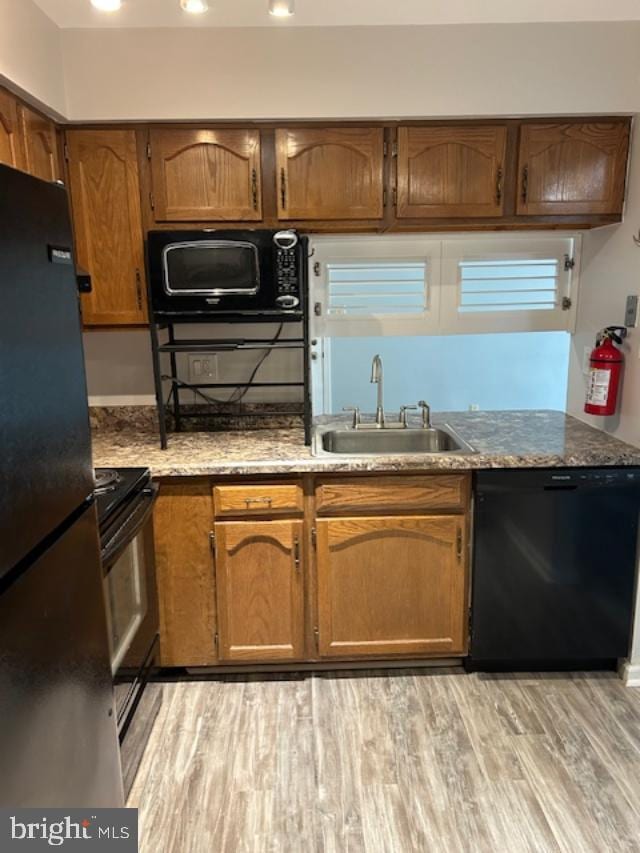 kitchen featuring light stone counters, light wood-style flooring, a sink, brown cabinets, and black appliances