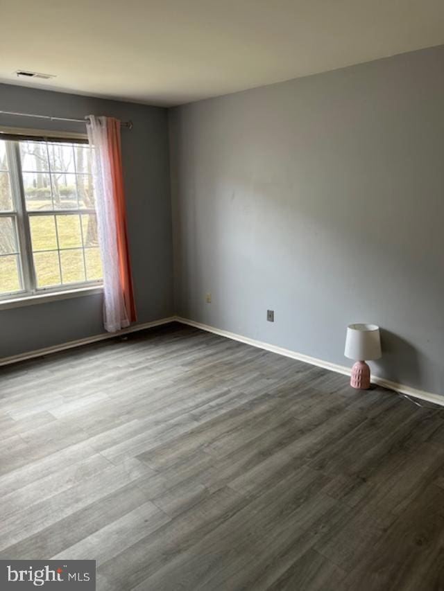 unfurnished room featuring dark wood-style floors, visible vents, and baseboards