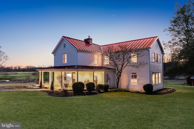 back of house at dusk featuring metal roof, a standing seam roof, a chimney, and a lawn