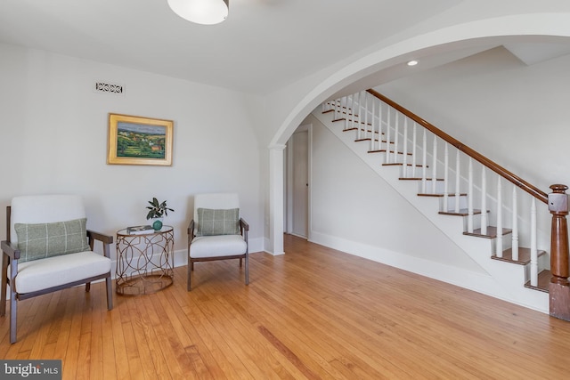 living area featuring visible vents, arched walkways, baseboards, hardwood / wood-style flooring, and stairway