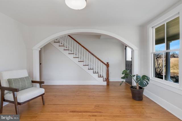 sitting room featuring arched walkways, light wood finished floors, stairway, and baseboards