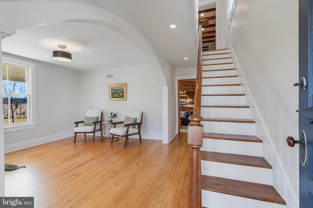 foyer featuring arched walkways, baseboards, light wood finished floors, and stairs