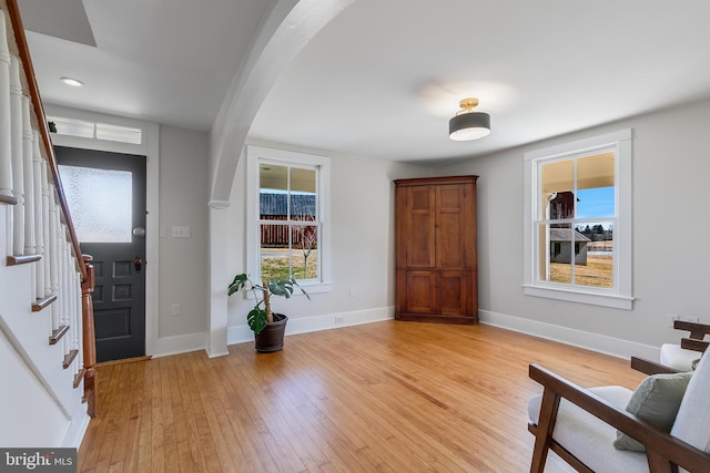 entryway with light wood finished floors, baseboards, stairway, and arched walkways