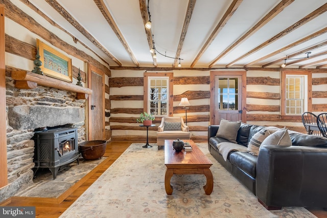 living area featuring a wood stove, beamed ceiling, track lighting, and wood finished floors