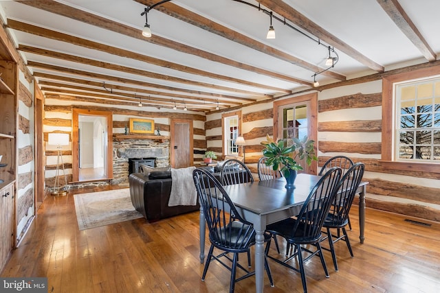 dining space featuring visible vents, beamed ceiling, hardwood / wood-style floors, log walls, and a stone fireplace