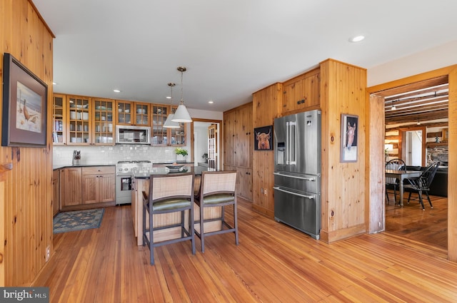 kitchen featuring a center island, a breakfast bar, appliances with stainless steel finishes, glass insert cabinets, and light wood-style floors