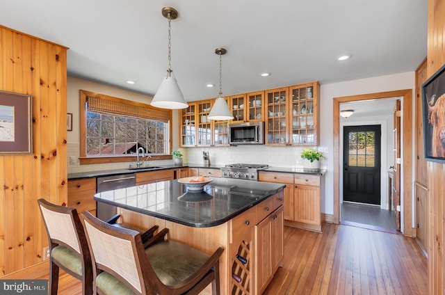 kitchen with stainless steel appliances, a sink, light wood-type flooring, decorative backsplash, and glass insert cabinets