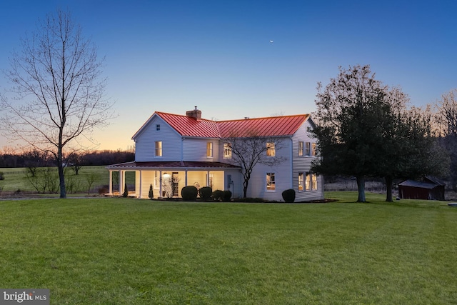 back of house at dusk featuring a standing seam roof, metal roof, a chimney, and a lawn