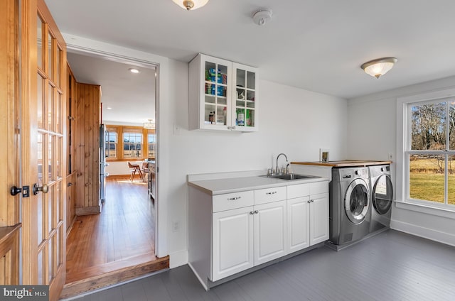 laundry room with dark wood-style floors, washing machine and clothes dryer, cabinet space, a sink, and baseboards