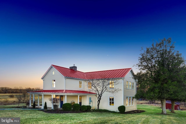 view of front of home with a yard, a chimney, covered porch, a standing seam roof, and metal roof