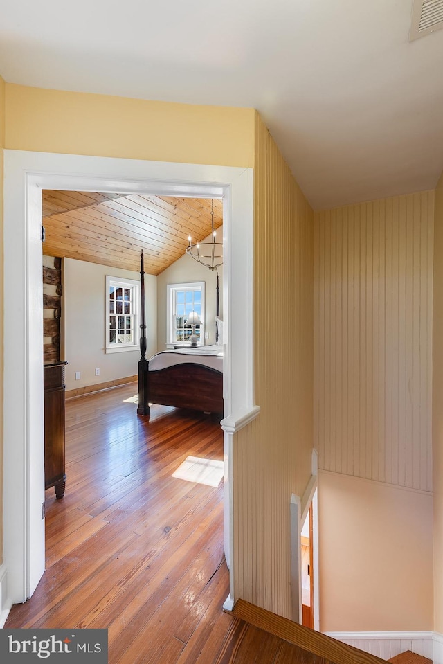 hall with visible vents, lofted ceiling, wood ceiling, hardwood / wood-style floors, and an upstairs landing