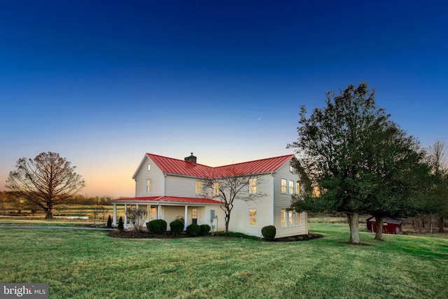 property exterior at dusk featuring an outbuilding, a yard, a chimney, a standing seam roof, and metal roof