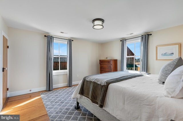 bedroom featuring multiple windows, wood finished floors, visible vents, and baseboards