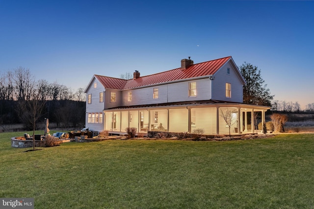 back of house at dusk featuring metal roof, an outdoor fire pit, a standing seam roof, and a lawn