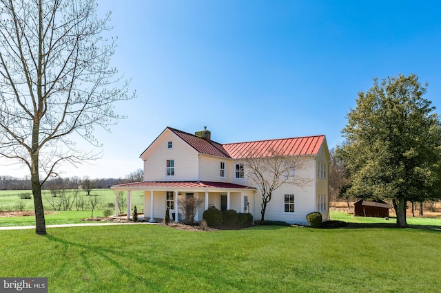 view of front of property with a chimney, metal roof, a standing seam roof, covered porch, and a front lawn