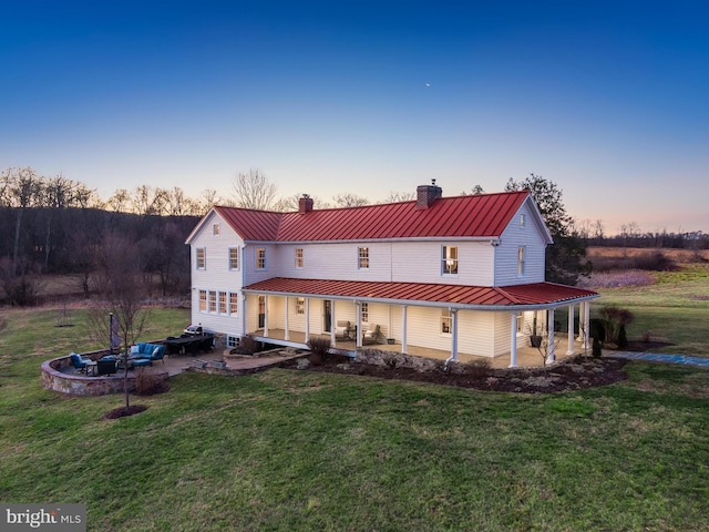 rear view of property with a patio, a chimney, a lawn, a standing seam roof, and metal roof