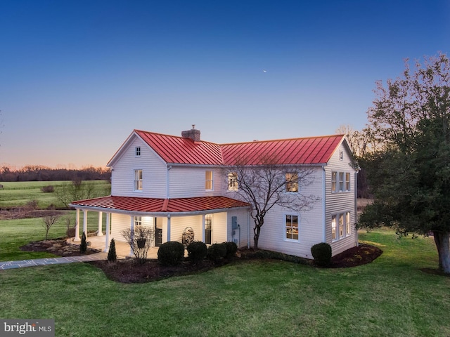 back of house at dusk featuring metal roof, a yard, a standing seam roof, and a chimney