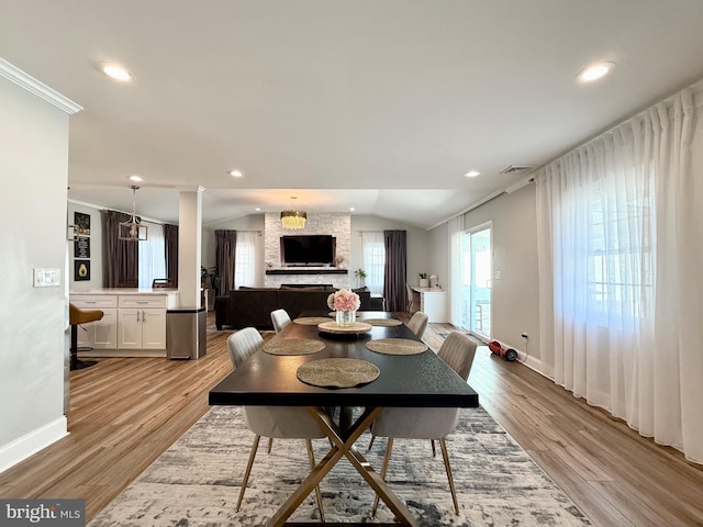 dining room with lofted ceiling, a stone fireplace, light wood-style flooring, and recessed lighting