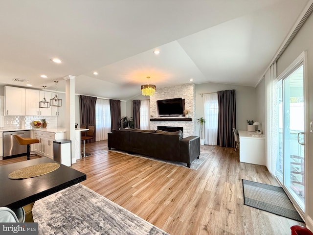 living area with vaulted ceiling, a fireplace, decorative columns, and light wood-style floors