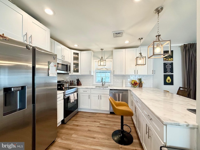 kitchen featuring visible vents, light wood-style flooring, a peninsula, stainless steel appliances, and a sink