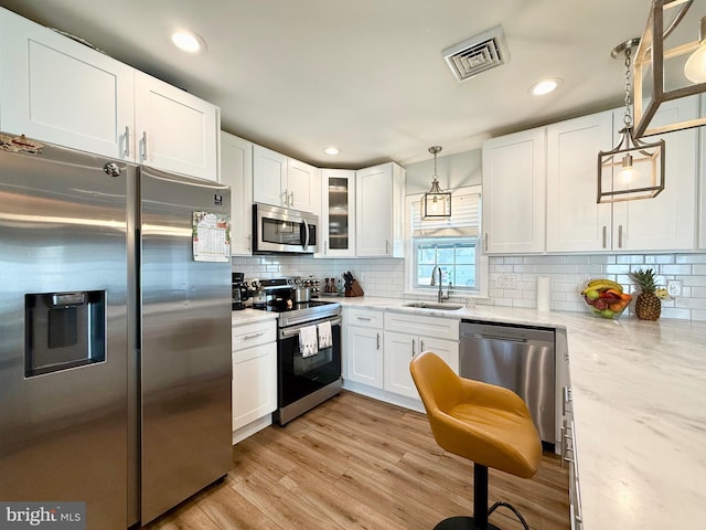 kitchen with visible vents, white cabinets, light wood-style flooring, stainless steel appliances, and a sink