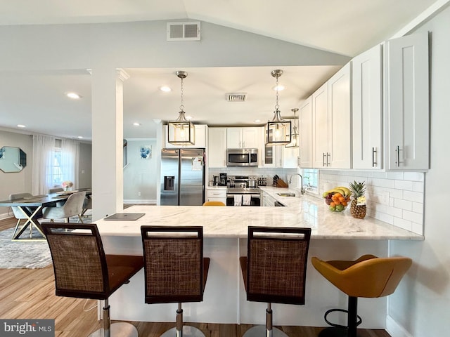 kitchen with light stone counters, a peninsula, a sink, visible vents, and appliances with stainless steel finishes