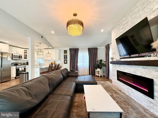 living area with visible vents, vaulted ceiling, a stone fireplace, a chandelier, and recessed lighting