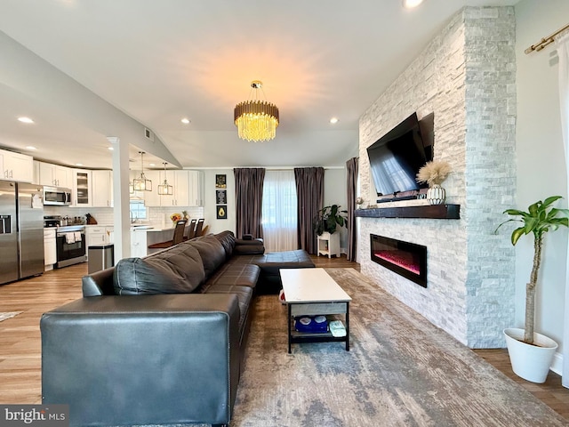 living room featuring vaulted ceiling, a stone fireplace, recessed lighting, and light wood-style floors