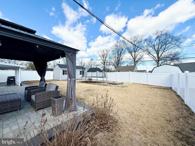 view of yard with a patio, a fenced backyard, an outbuilding, a trampoline, and a shed