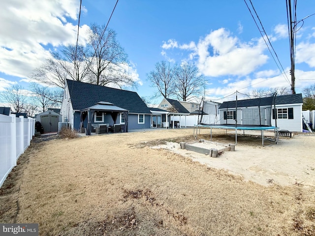 rear view of house featuring a trampoline, a storage unit, fence, and an outdoor structure