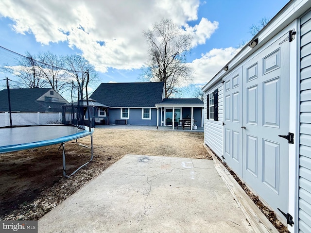 back of house featuring a shingled roof, a trampoline, and a patio