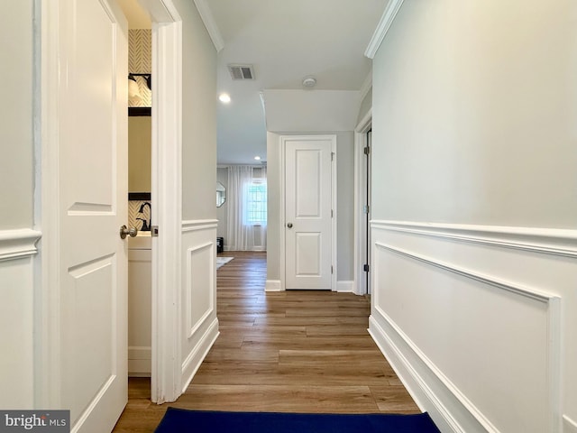 hallway with ornamental molding, wood finished floors, visible vents, and baseboards