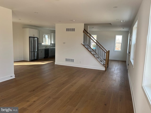 unfurnished living room featuring stairway, plenty of natural light, visible vents, and dark wood-type flooring