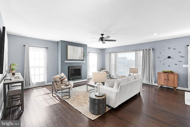 living room featuring a glass covered fireplace, plenty of natural light, dark wood-style floors, and baseboards