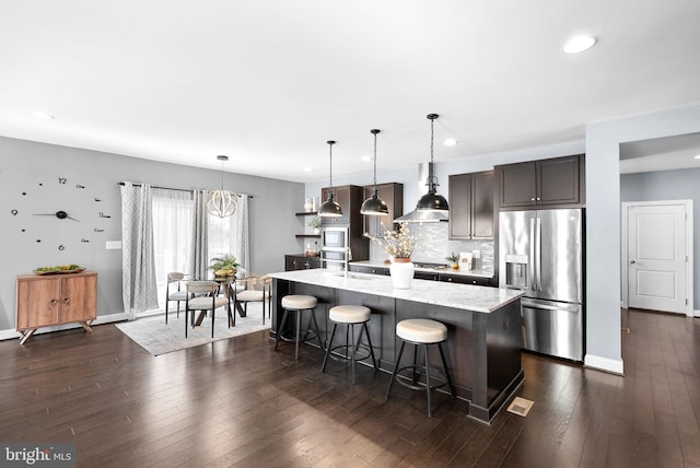 kitchen featuring dark wood finished floors, a breakfast bar area, wall chimney exhaust hood, and appliances with stainless steel finishes