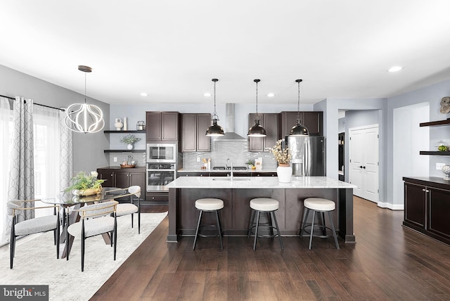 kitchen with open shelves, appliances with stainless steel finishes, a sink, and wall chimney range hood