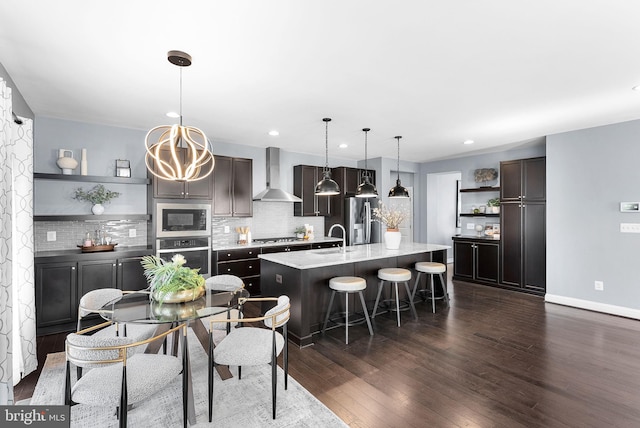 kitchen featuring a kitchen island with sink, open shelves, a sink, stainless steel appliances, and wall chimney exhaust hood