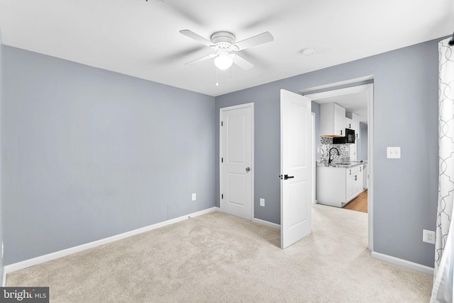 unfurnished bedroom featuring a ceiling fan, light colored carpet, baseboards, and a sink