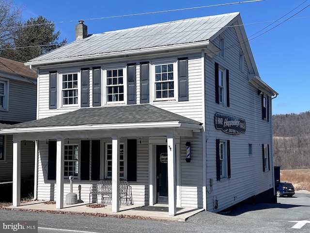 view of front facade featuring covered porch, metal roof, and a chimney