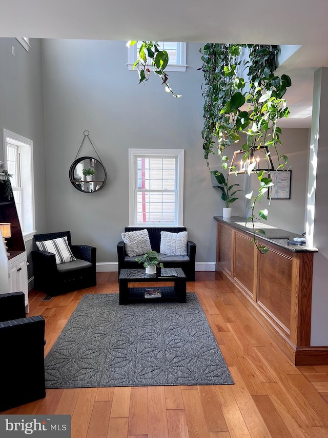 living area with light wood-type flooring, a towering ceiling, and baseboards