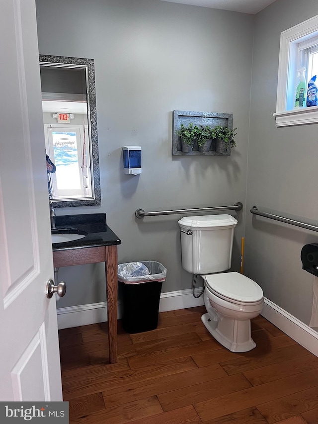 bathroom featuring baseboards, wood finished floors, toilet, and a healthy amount of sunlight