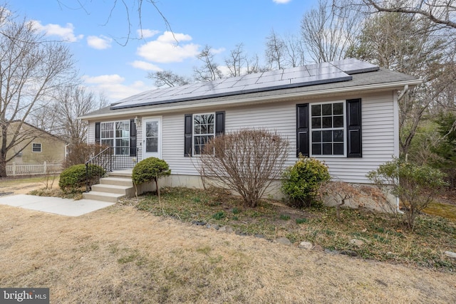 ranch-style house with a front yard, roof mounted solar panels, and fence