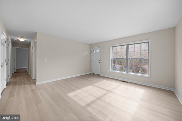 unfurnished living room featuring light wood finished floors, attic access, visible vents, and baseboards