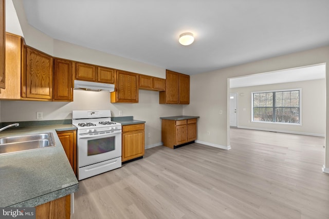 kitchen with under cabinet range hood, white gas range oven, brown cabinets, and a sink