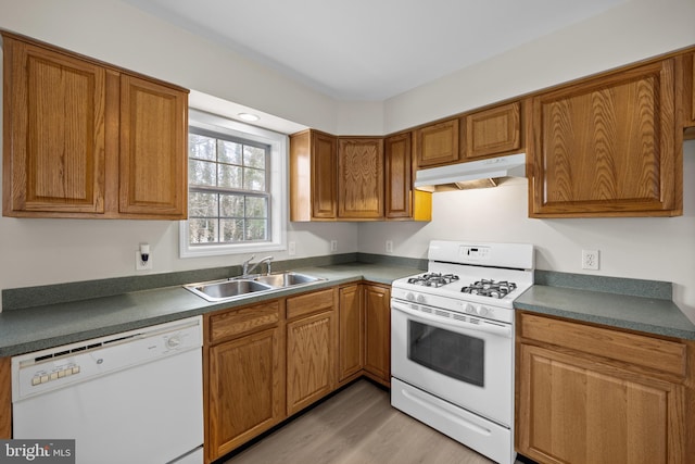 kitchen featuring under cabinet range hood, white appliances, a sink, light wood-type flooring, and brown cabinetry