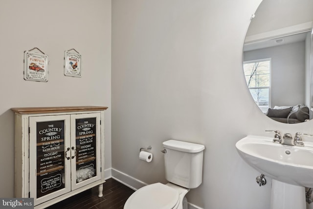 half bathroom with a sink, toilet, baseboards, and wood finished floors