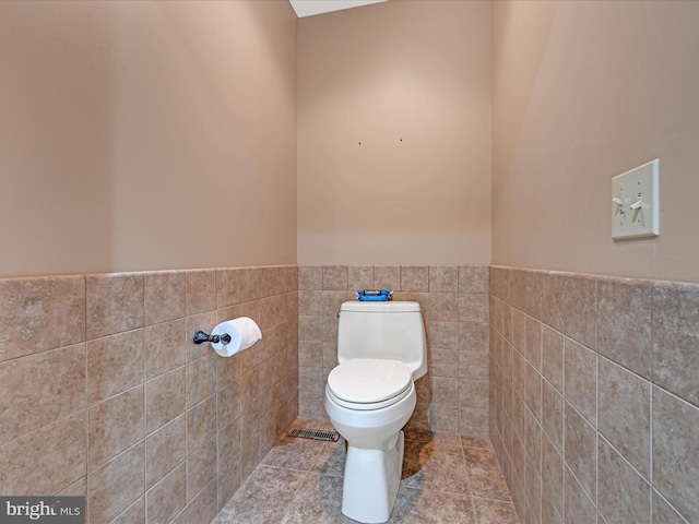 half bath featuring a wainscoted wall, tile walls, visible vents, toilet, and tile patterned flooring