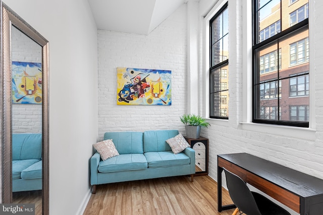 living area featuring a wealth of natural light, brick wall, and wood finished floors